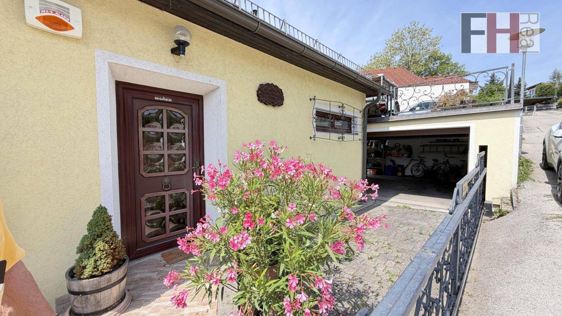 Eingangsbereich des Hauses mit blühenden Pflanzen und angrenzender offener Garage.