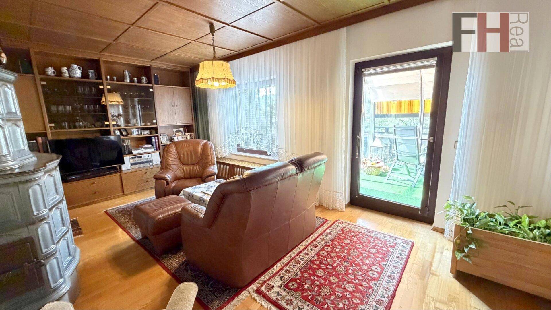 Wohnzimmer mit bequemen Ledersofas, Holzboden und Zugang zu einem Wintergarten oder Balkon.