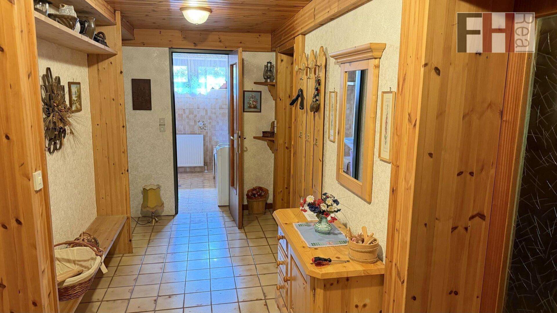 Heller Flur mit Holzvertäfelung, Fliesenboden und einem Spiegel, der zum Badezimmer führt.