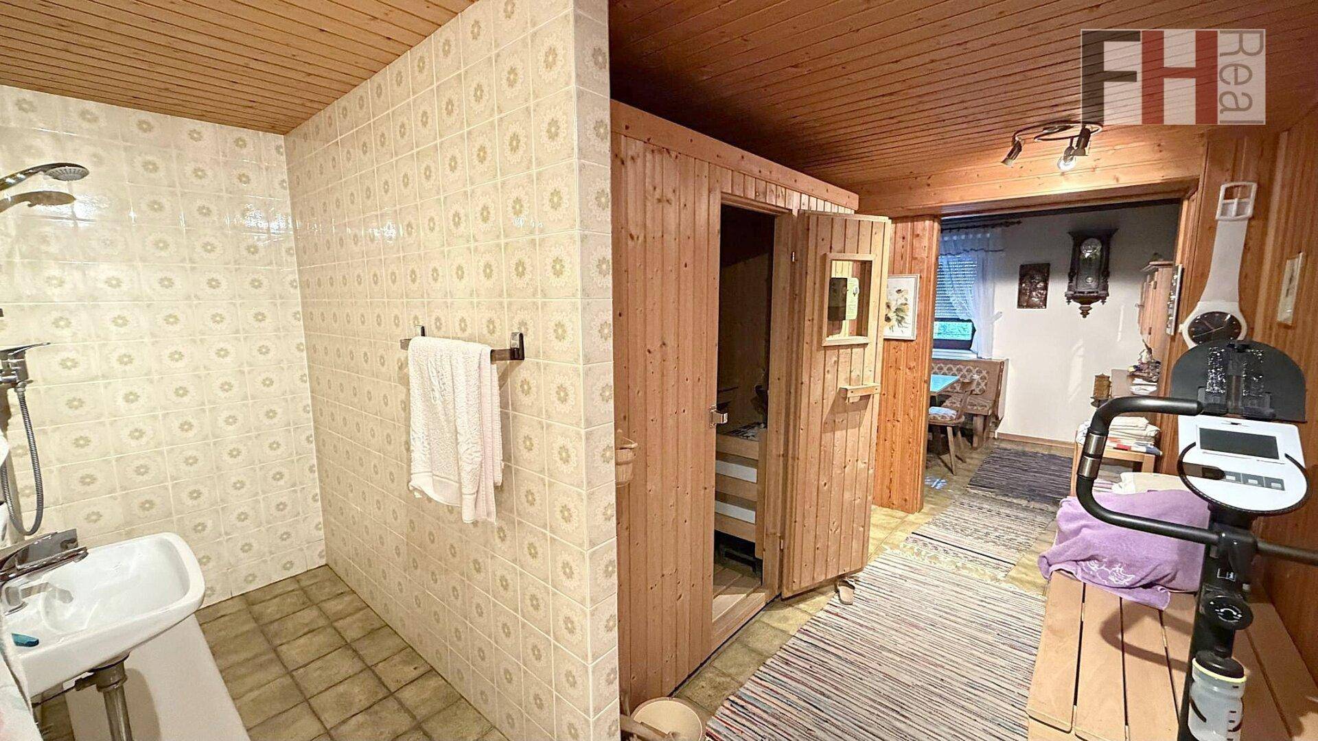 Badezimmer mit Dusche, Waschbecken und angrenzender Sauna, ideal für Wellness zu Hause.