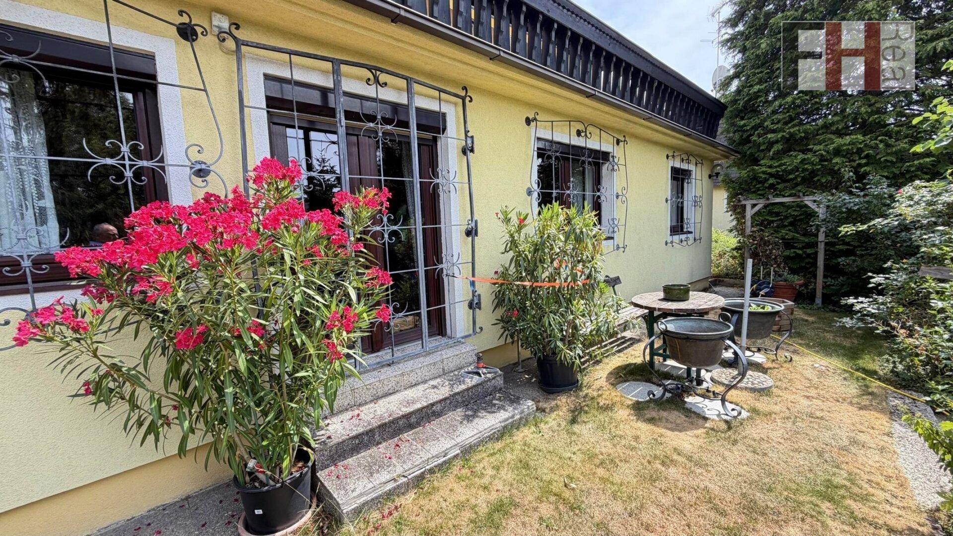 Kleiner Gartenbereich mit blühenden Pflanzen, Sitzgelegenheiten und Zugang zum Haus.