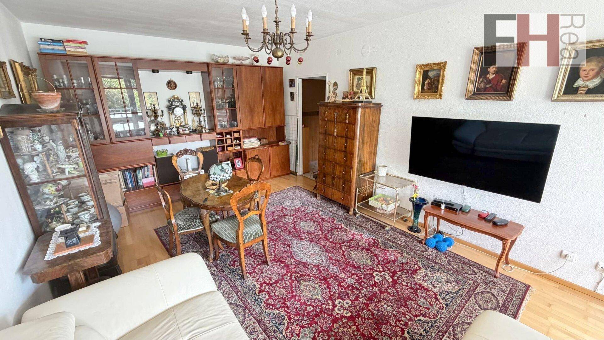 Gemütlicher Wohn- und Essbereich mit Fernseher, Kronleuchter und klassischem Teppich.