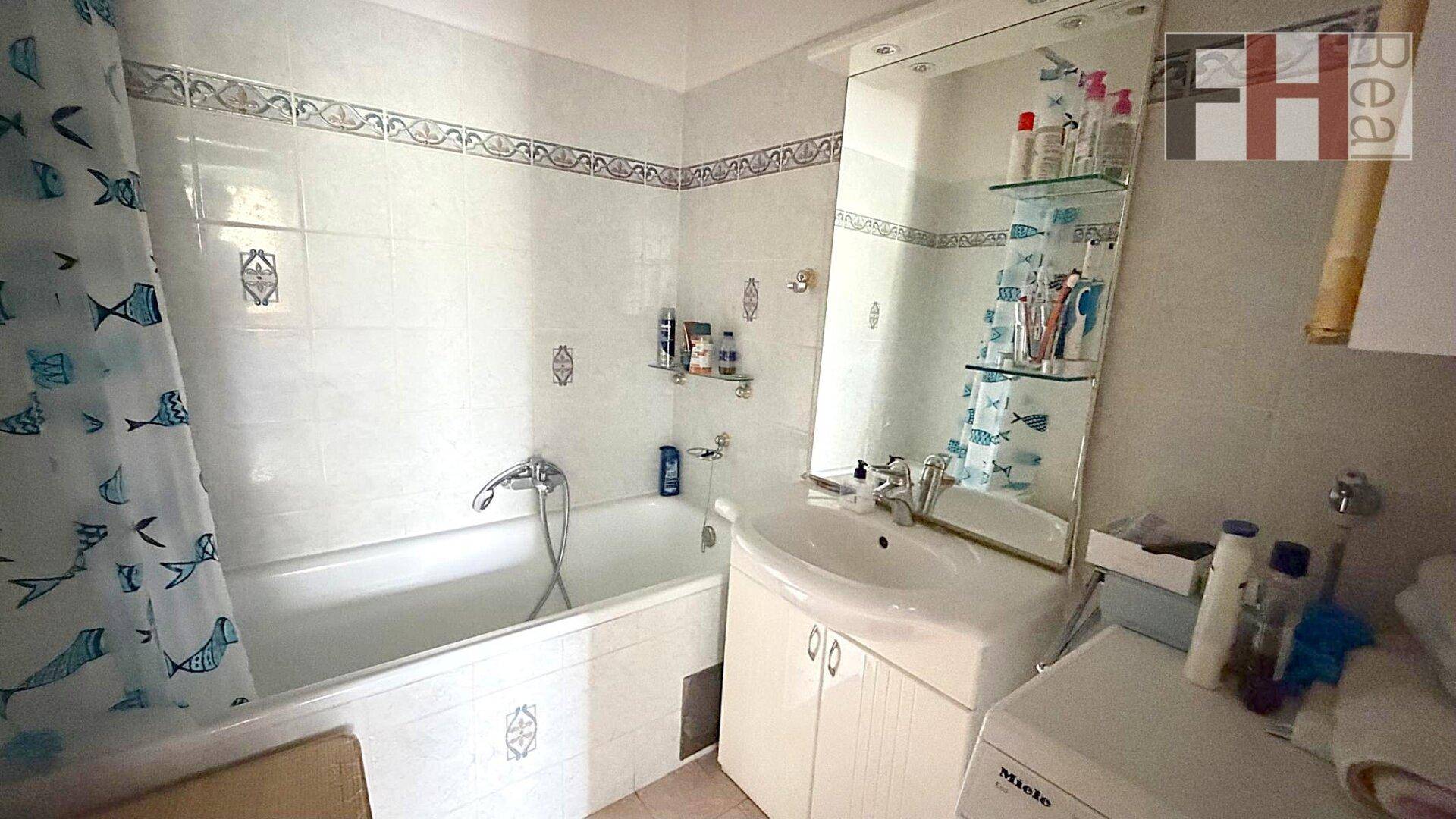 Badezimmer mit Badewanne, Waschbecken, Spiegelschrank und Waschmaschine.