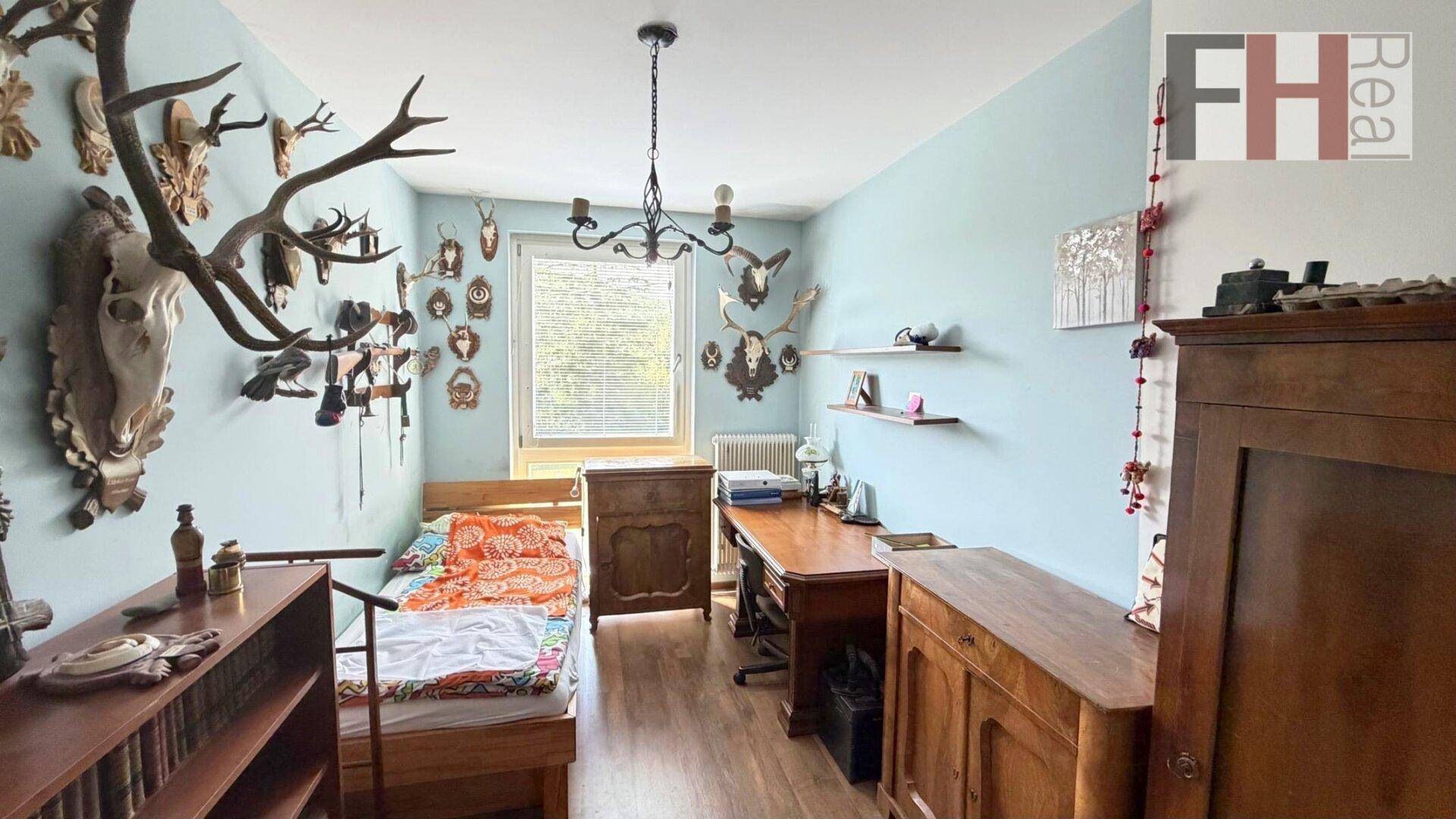 Schlafzimmer mit hellblauen Wänden, Holzmöbeln und traditioneller Hirschgeweih-Dekoration.