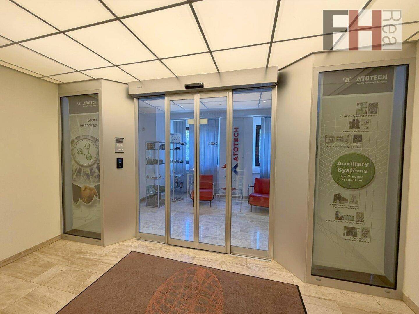 Moderner Eingangsbereich mit automatischen Glastüren und Informationsdisplays, einladend und funktional gestaltet.