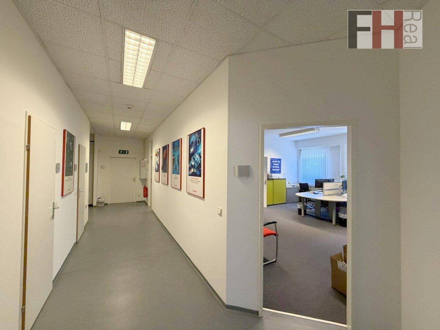 Langer Flur mit hellen Wänden, grauem Boden und mehreren Türen, der zu Büros führt.