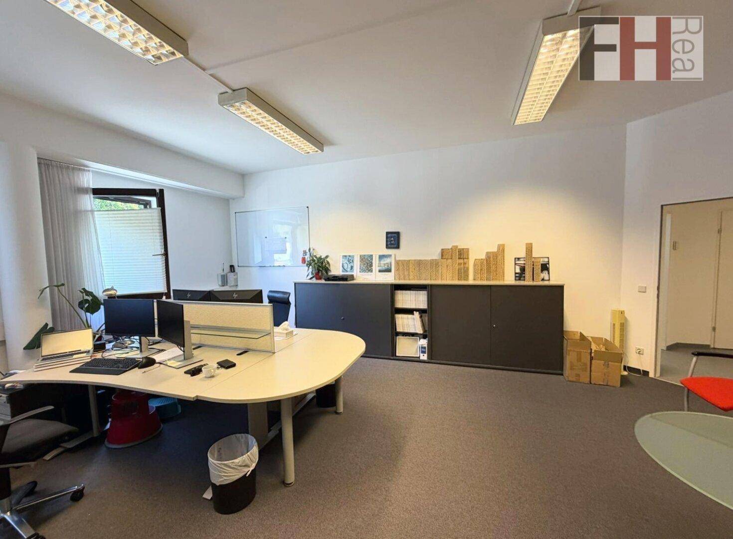 Geräumiges Büro mit mehreren Arbeitsplätzen, Schreibtischen, Büroschränken und Teppichboden.