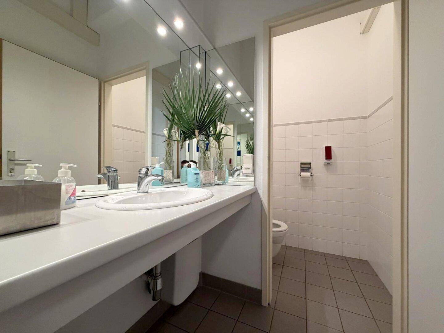 Damen-WC mit Waschbecken, großem Spiegel und Toilette, sauber und funktional eingerichtet.