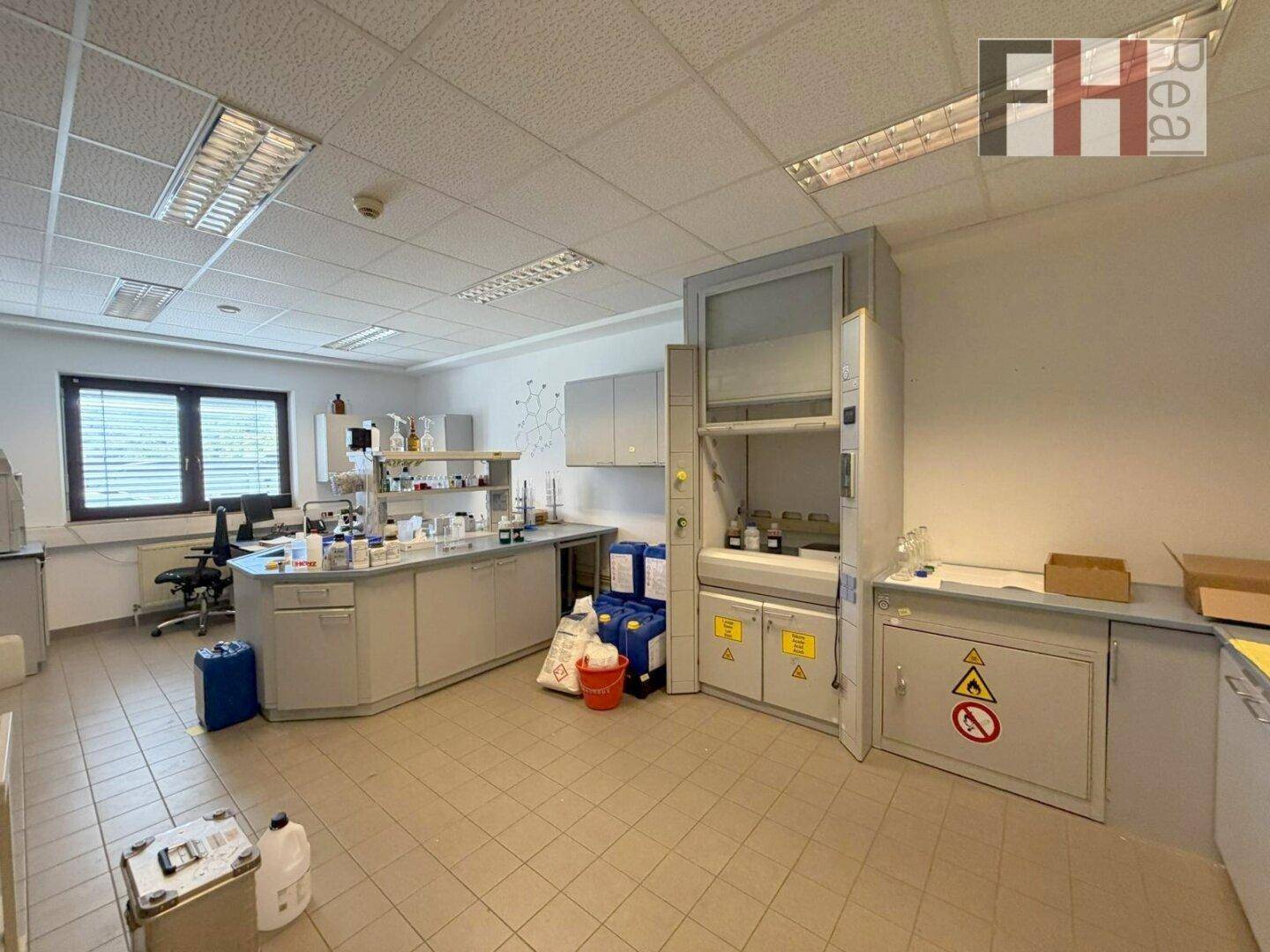Geräumiges Labor mit Arbeitsflächen, Abzügen und verschiedenen Geräten für wissenschaftliche Arbeiten.