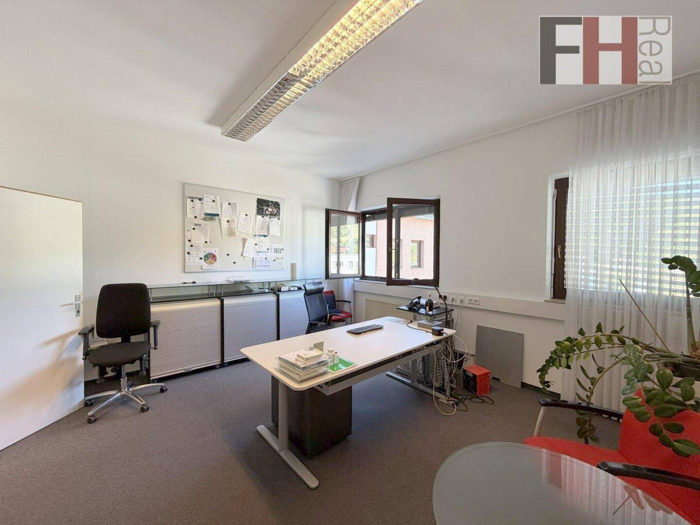 Büro mit Schreibtisch, Bürostuhl und Fenstern, die viel Tageslicht hereinlassen und eine angenehme Atmosphäre schaffen.