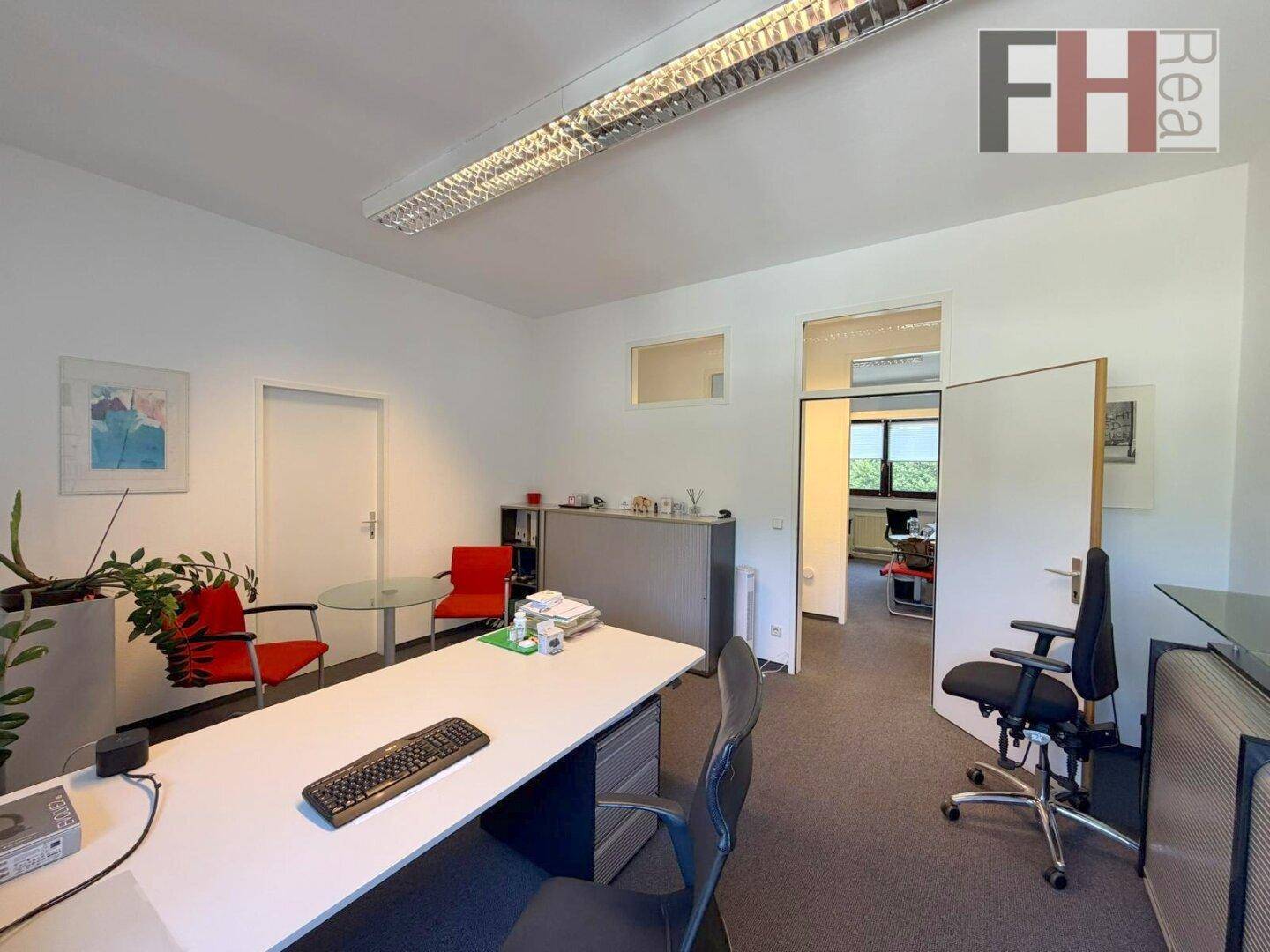 Büro mit Schreibtisch, Bürostuhl und einem offenen Durchgang zu einem weiteren Raum, ideal für Teamarbeit.