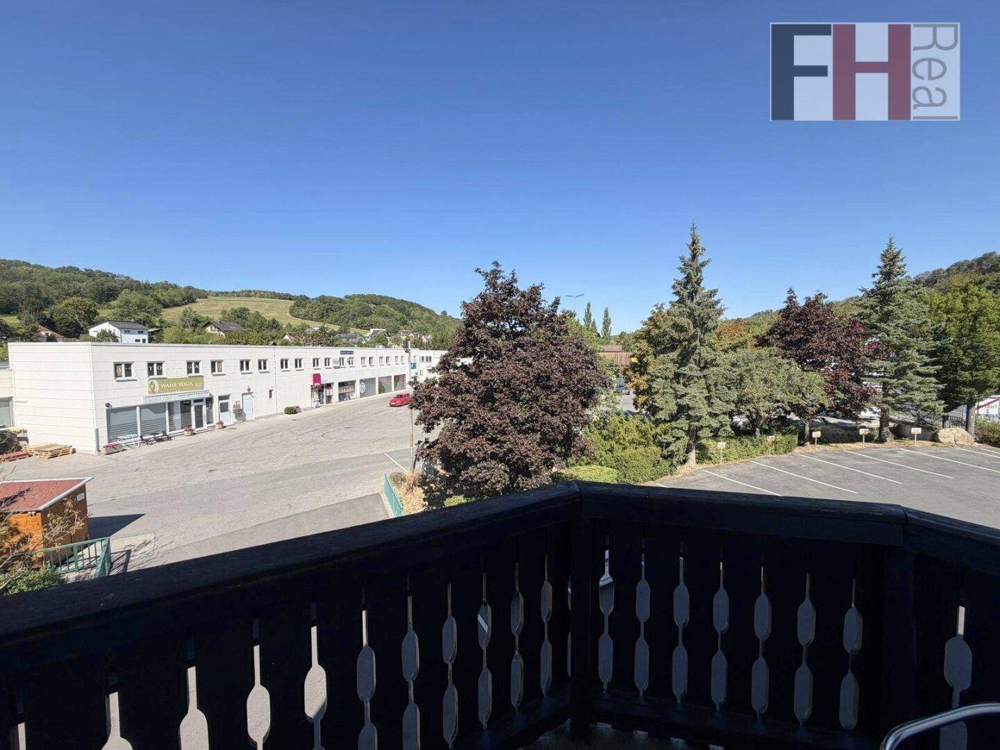 Balkon mit Holzbalkongeländer und weitem Blick auf die umliegende Landschaft und Gebäude.