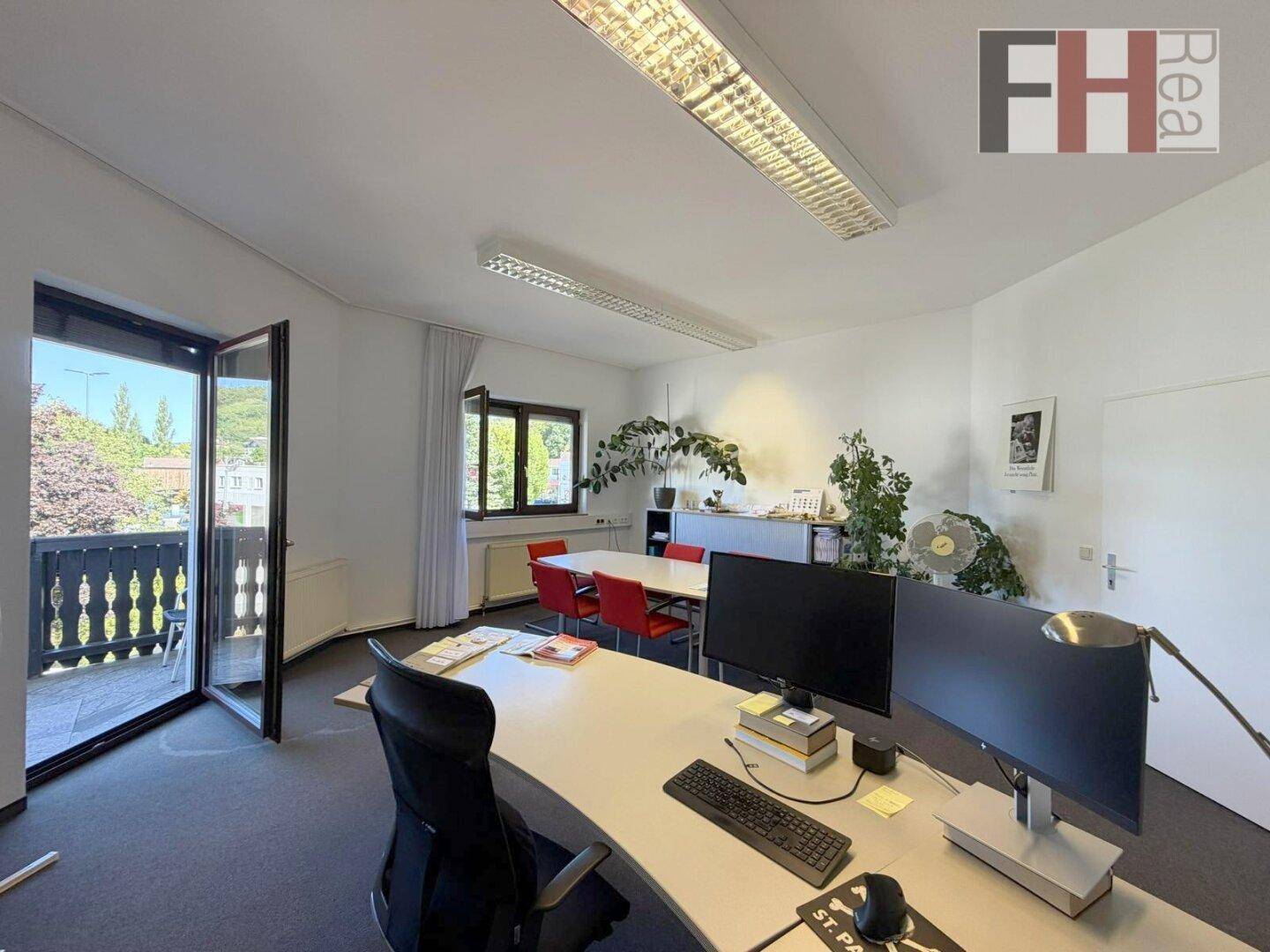 Helles Büro mit Schreibtisch, Computer und Zugang zu einem Balkon mit Blick ins Grüne.
