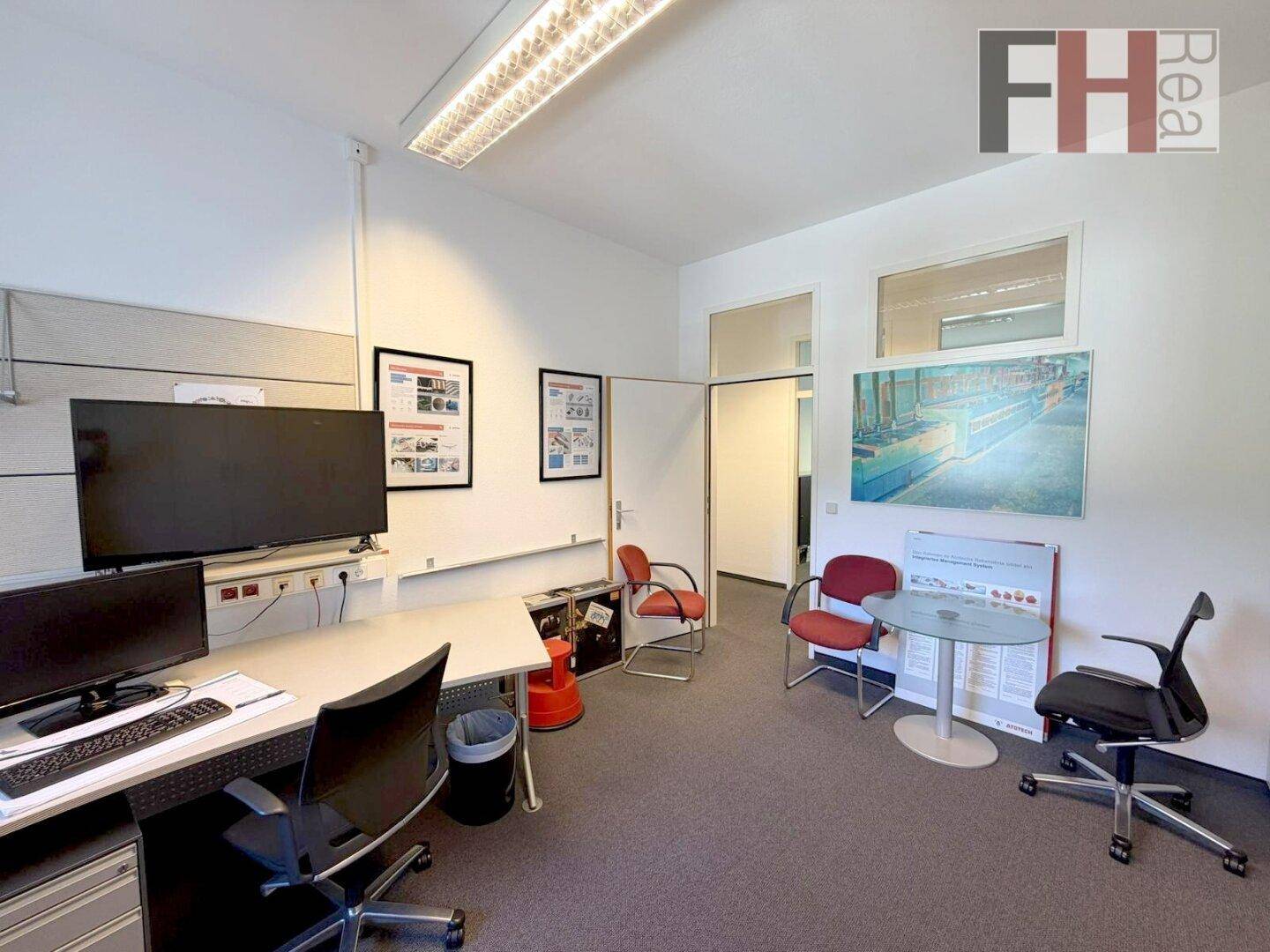 Büro mit mehreren Arbeitsplätzen, einem Fernseher und einem kleinen Besprechungsbereich.