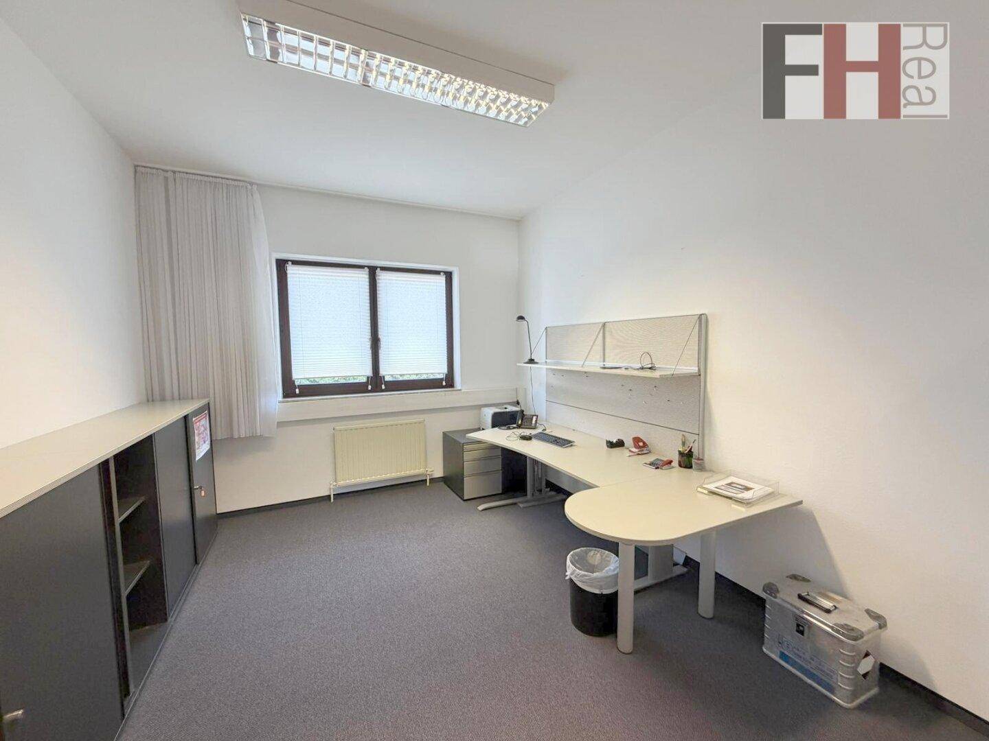 Geräumiges Büro mit Schreibtisch, Büroschränken und einem großen Fenster.