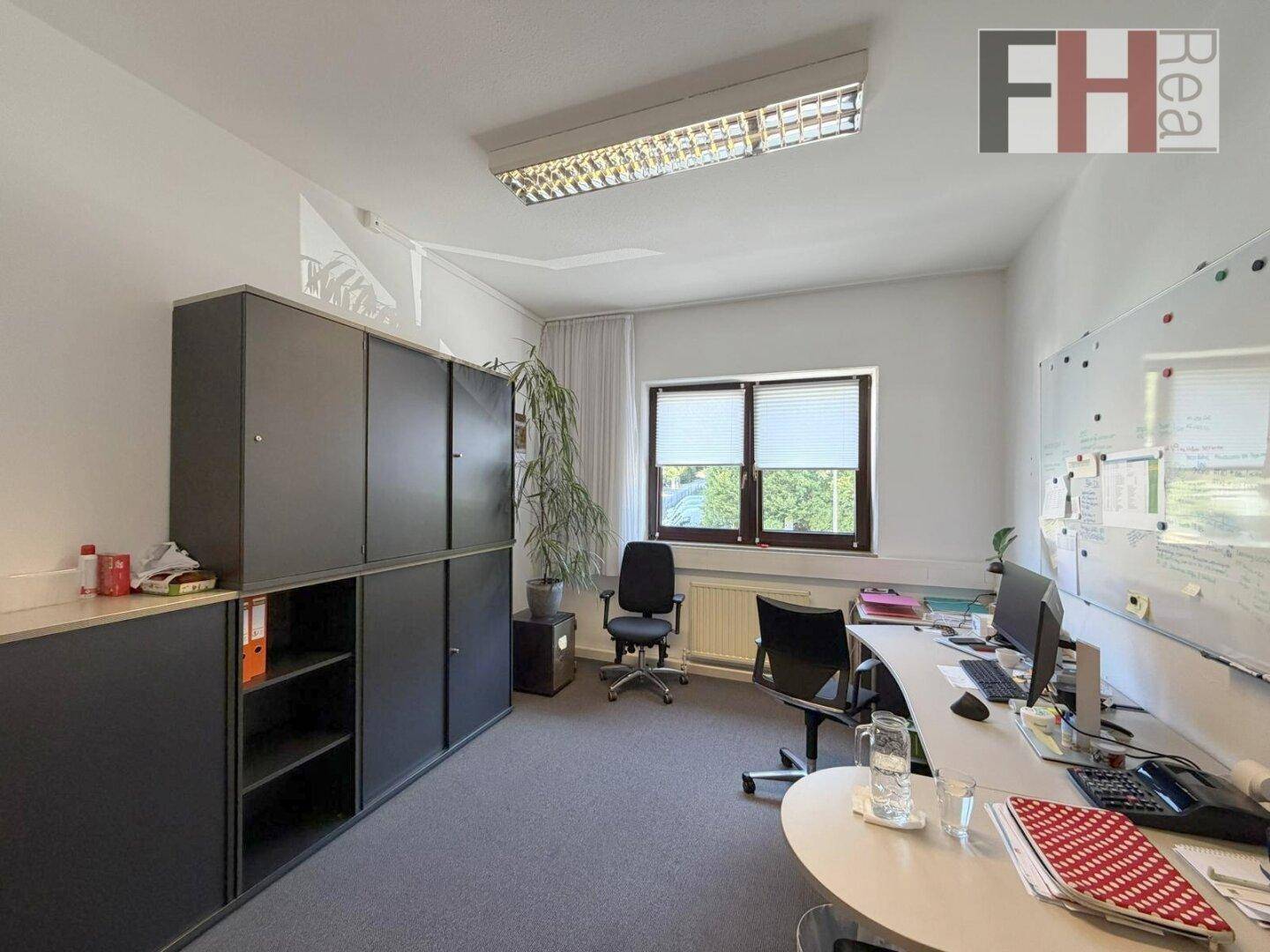Büro mit dunklen Aktenschränken, Schreibtisch und einem Fenster mit Jalousien.