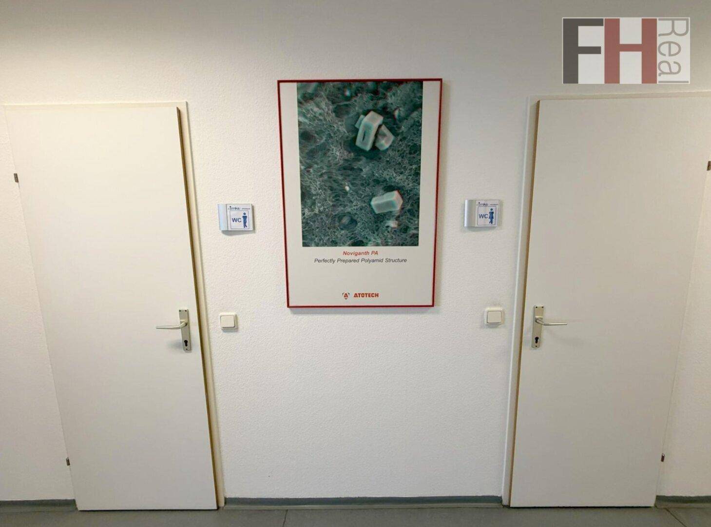 Flur mit zwei Türen zu Toiletten und einem gerahmten Bild an der Wand.