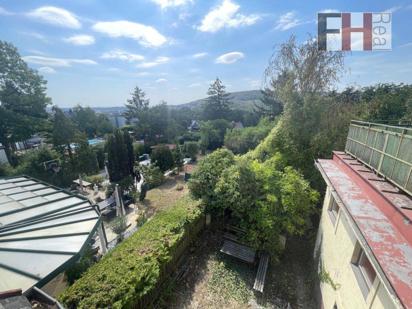 Weitläufiger Blick über einen verwilderten Garten, benachbarte Grundstücke und die hügelige Landschaft.