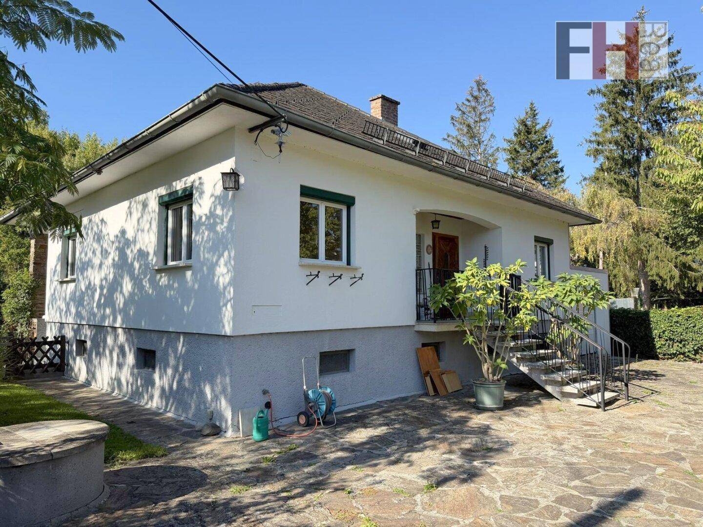 Seitenansicht des Hauses mit weißer Fassade, grauer Sockelzone und gepflastertem Bereich.