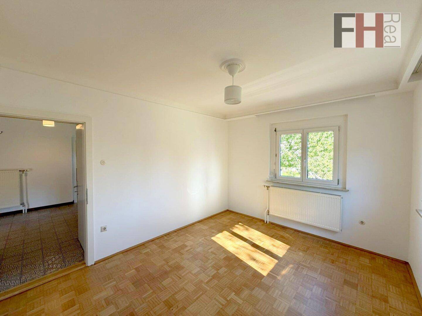 Geräumiges Schlafzimmer mit Parkettboden und Blick ins Grüne, ideal für Ruhe und Entspannung.