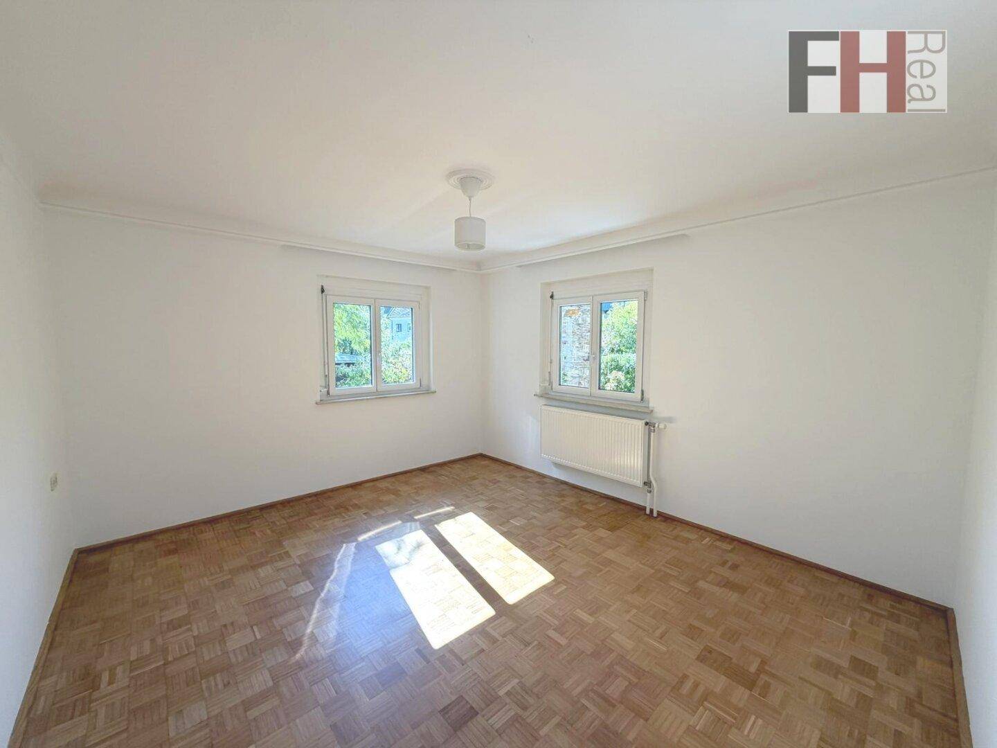 Helles Schlafzimmer mit Parkettboden und zwei Fenstern, die eine angenehme Atmosphäre schaffen.