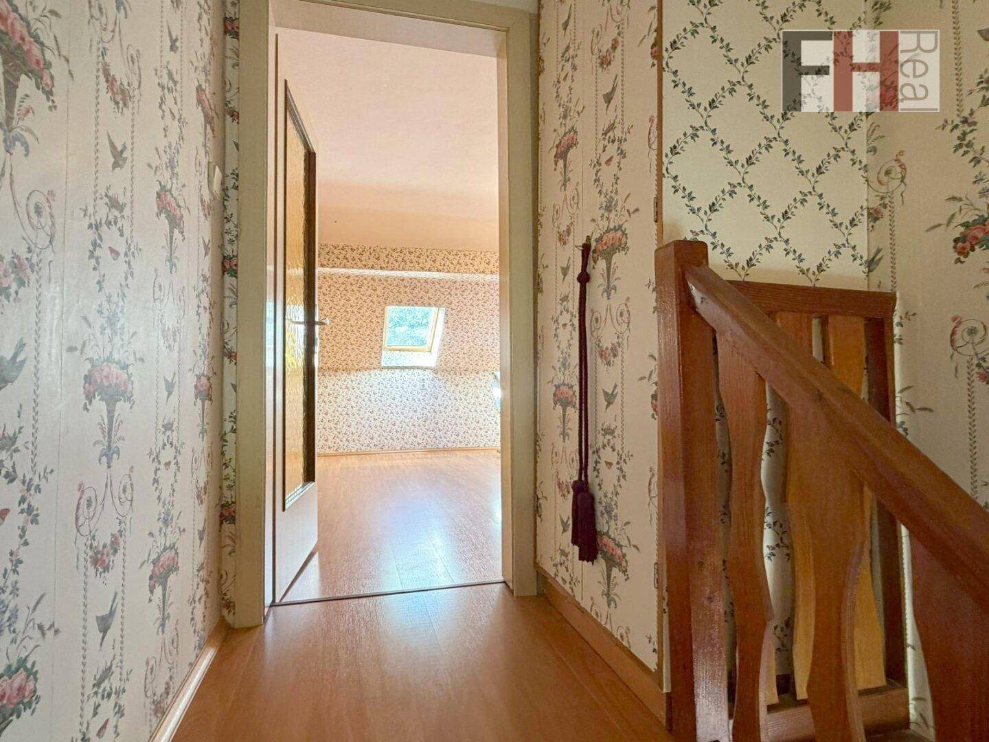 Flur mit Holzfußboden und gemusterter Tapete, der zu einem weiteren Zimmer führt.