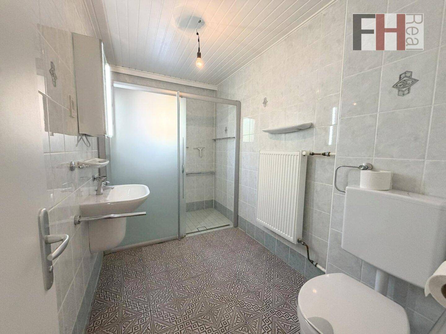Gefliestes Badezimmer mit Dusche, WC und Waschbecken, funktional und hell.