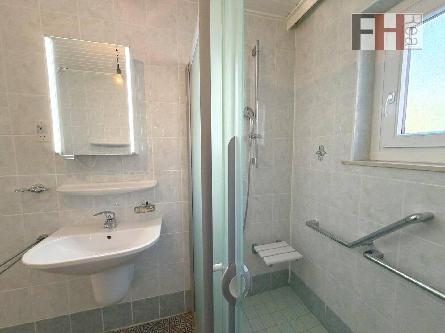Modernes Badezimmer mit Duschkabine, Waschbecken und Fenster, ausgestattet mit Haltegriffen.