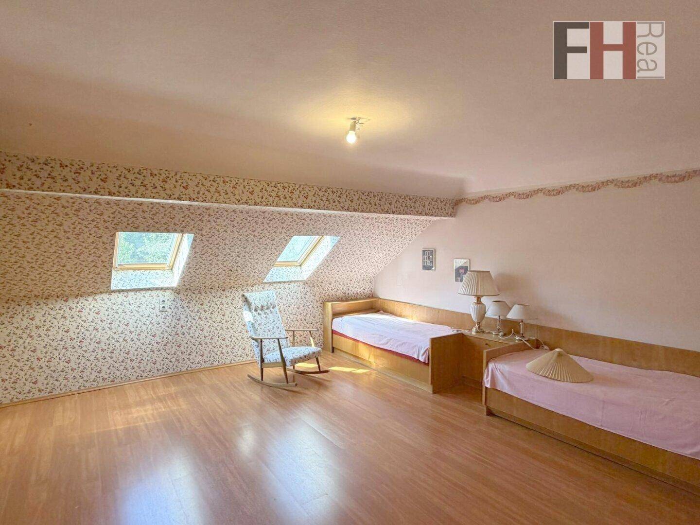 Gemütliches Schlafzimmer im Dachgeschoss mit Dachfenstern, Holzfußboden und floraler Tapete.