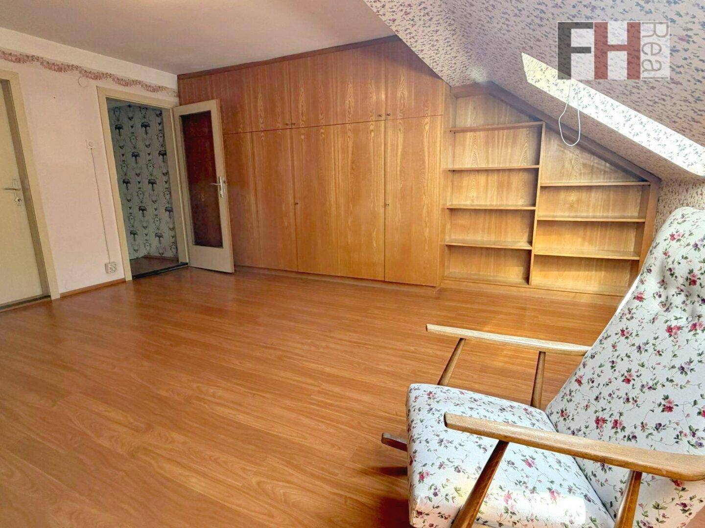 Dachgeschosszimmer mit Holzfußboden, Einbauschränken und Regalen unter der Dachschräge.