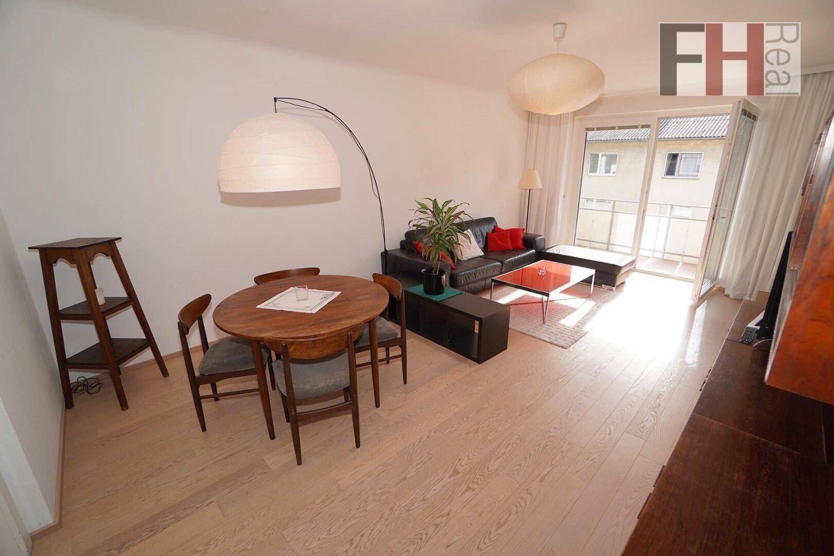 Heller Wohn- und Essbereich mit Holztisch und Zugang zu einem sonnigen Balkon.