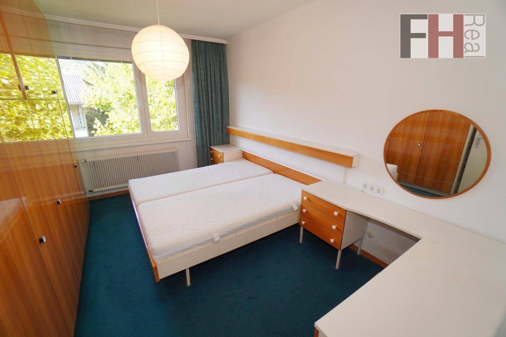 Schlafzimmer mit zwei Einzelbetten, Holzmöbeln und großem Fenster für viel Tageslicht.