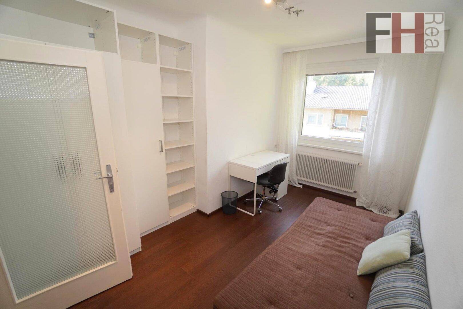 Helles Schlafzimmer mit Schreibtisch, integrierten Regalen und Fenster mit Ausblick.