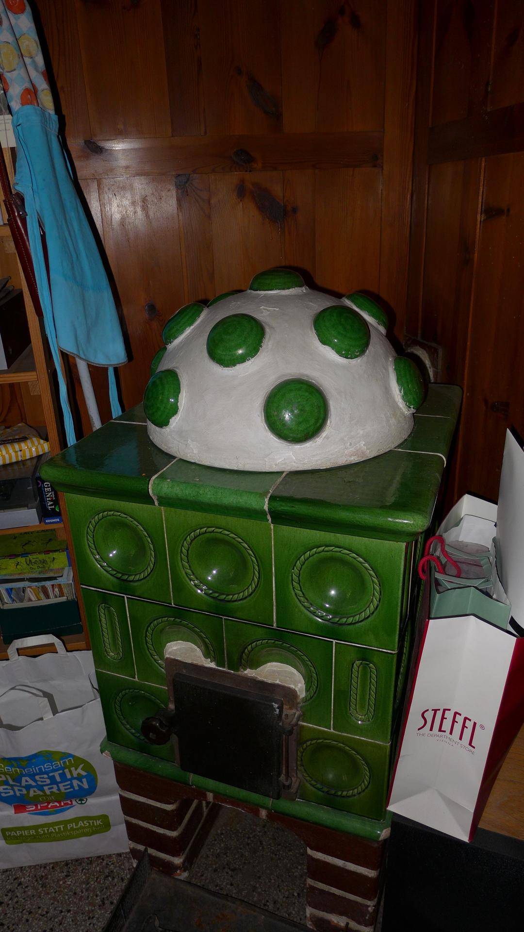 Detailaufnahme eines traditionellen grünen Kachelofens mit dekorativer Haube.