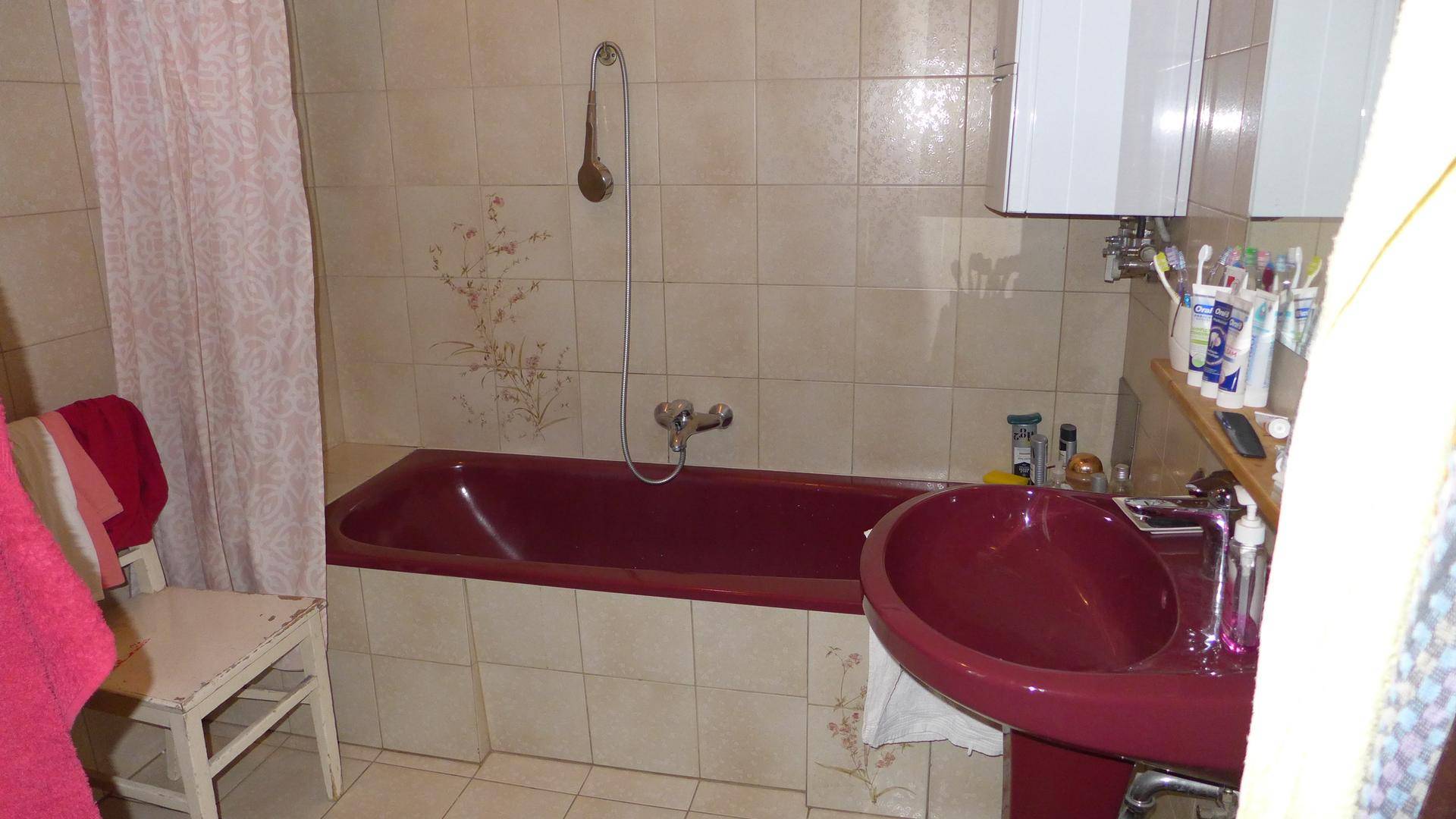 Badezimmer mit beigen Fliesen, weinroter Badewanne und passendem Waschbecken.