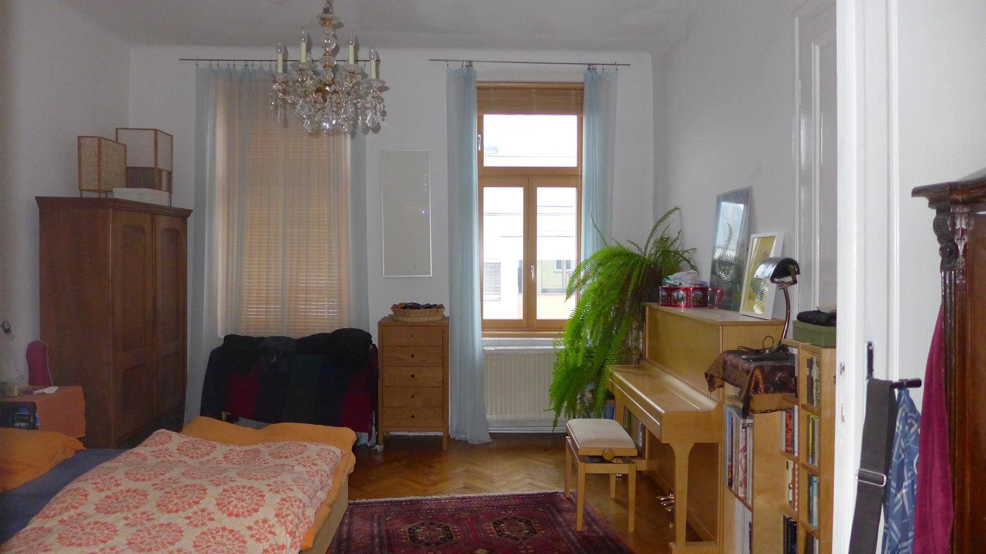 Helles Schlafzimmer mit Holzbett, Klavier, Parkettboden und zwei Fenstern.