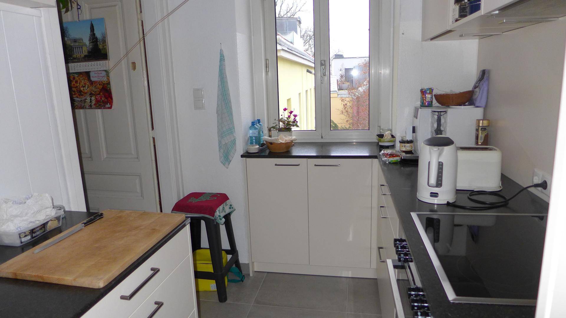 Helle Küche mit weißen Unterschränken, schwarzer Arbeitsplatte und Fenster.
