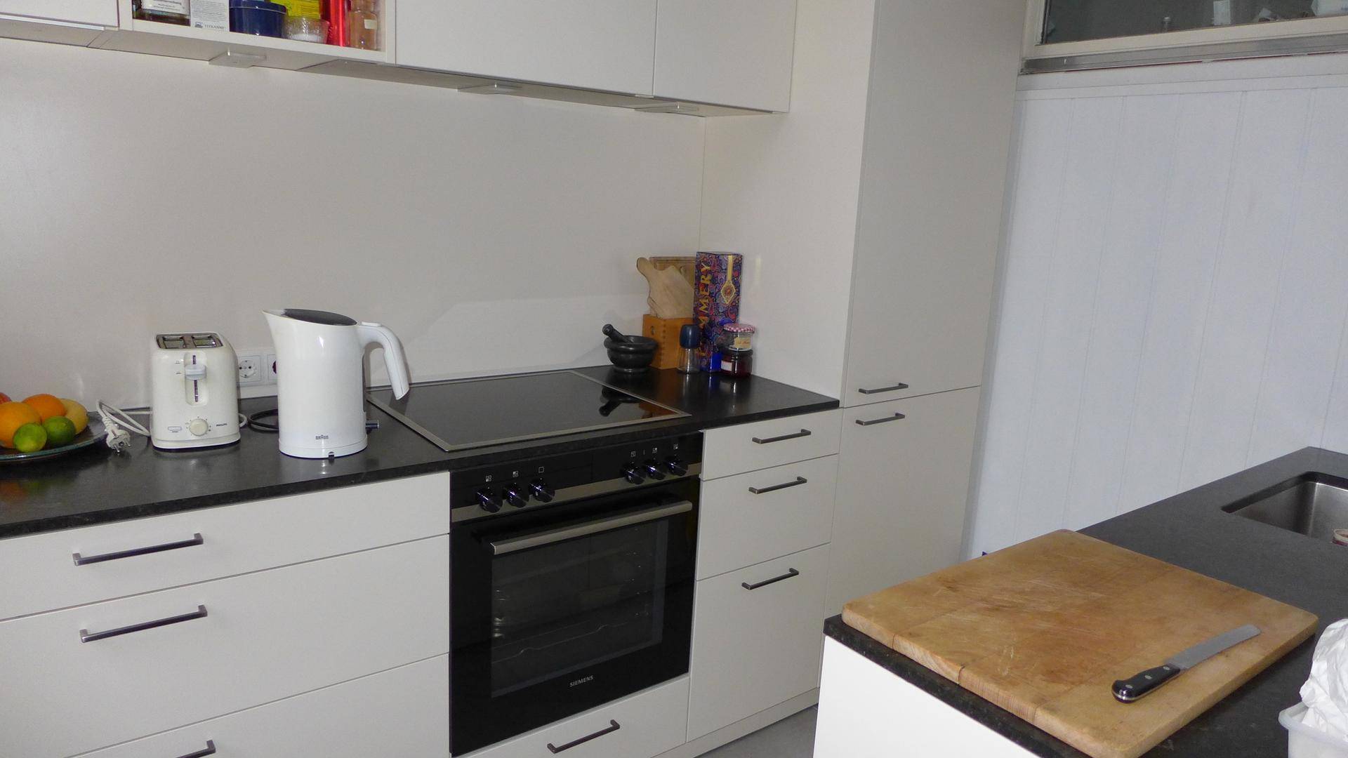 Moderne Küche mit weißen Schränken, schwarzer Arbeitsplatte und integriertem Kochfeld und Backofen.