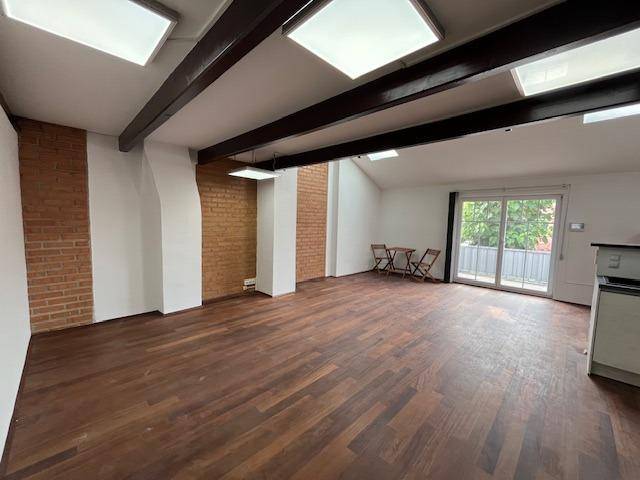 Heller Wohnbereich mit Holzboden, freiliegenden Ziegelwänden und Zugang zum Balkon.