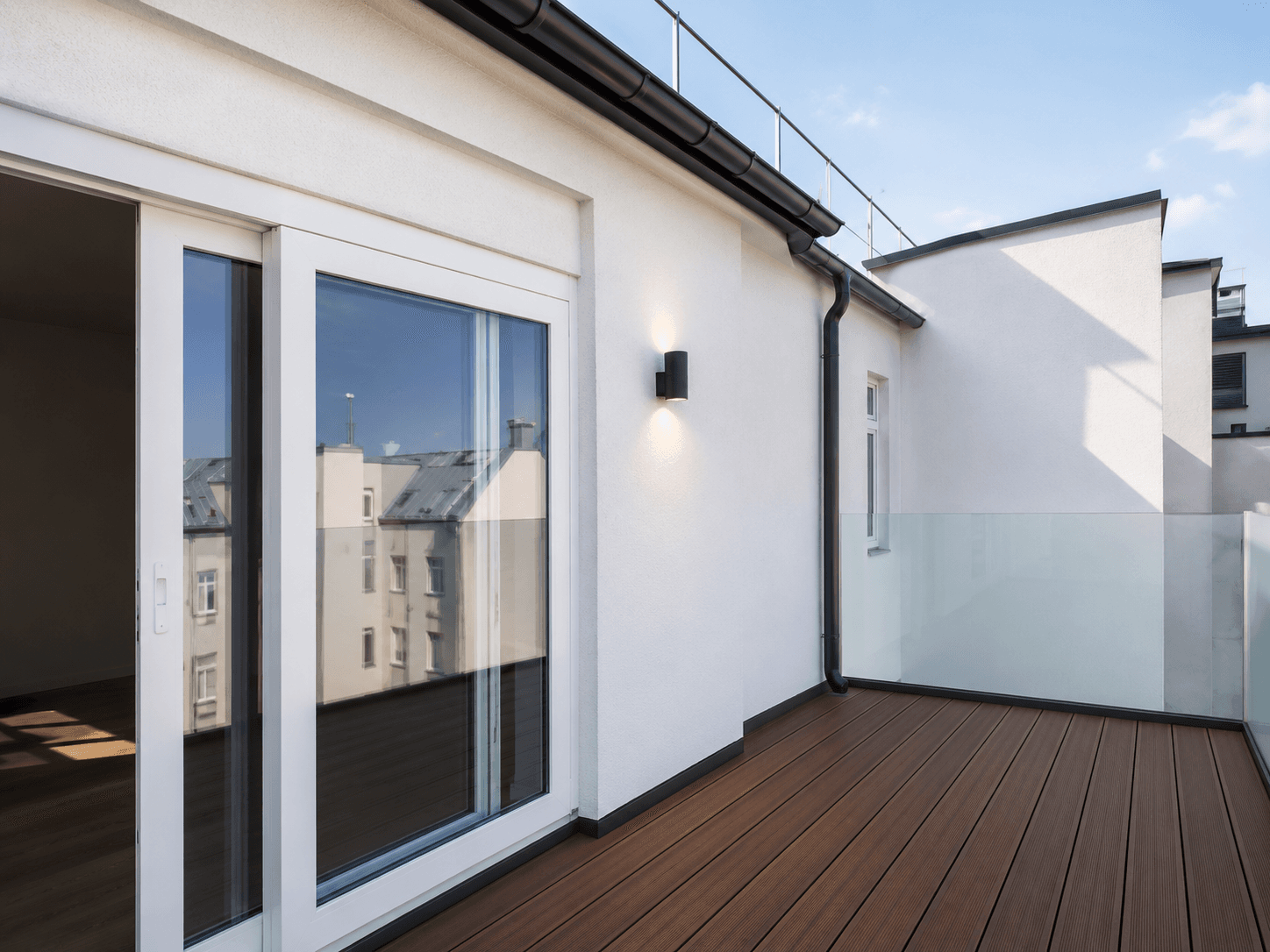 Moderner Balkon mit Holzboden und Glasgeländer, zugänglich durch eine große Schiebetür, bietet einen Blick auf die Umgebung.