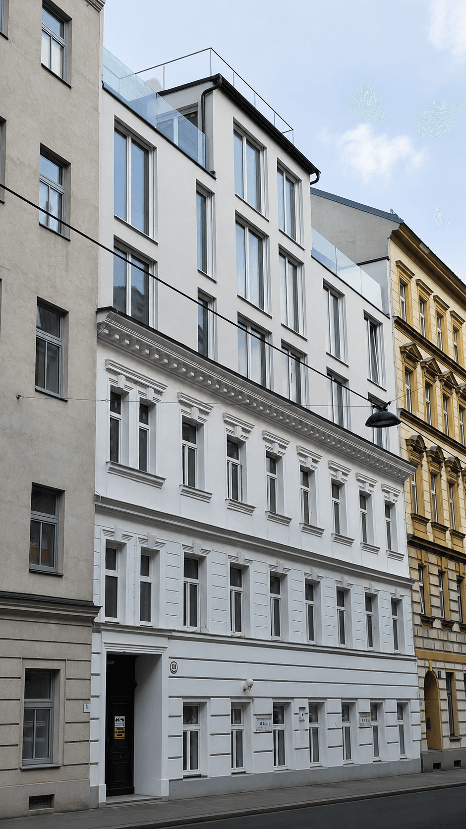 Fassade eines modernen Gebäudes mit großen Fenstern, integriert in eine historische Straßenzeile mit Altbauten.