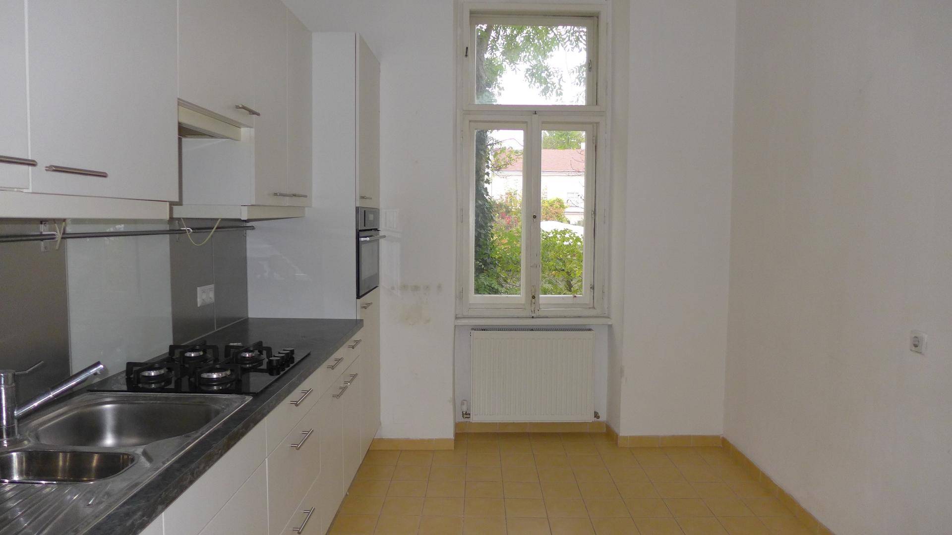 Helle Küche mit weißen Schränken, Gasherd und einem Fenster mit Blick ins Grüne.