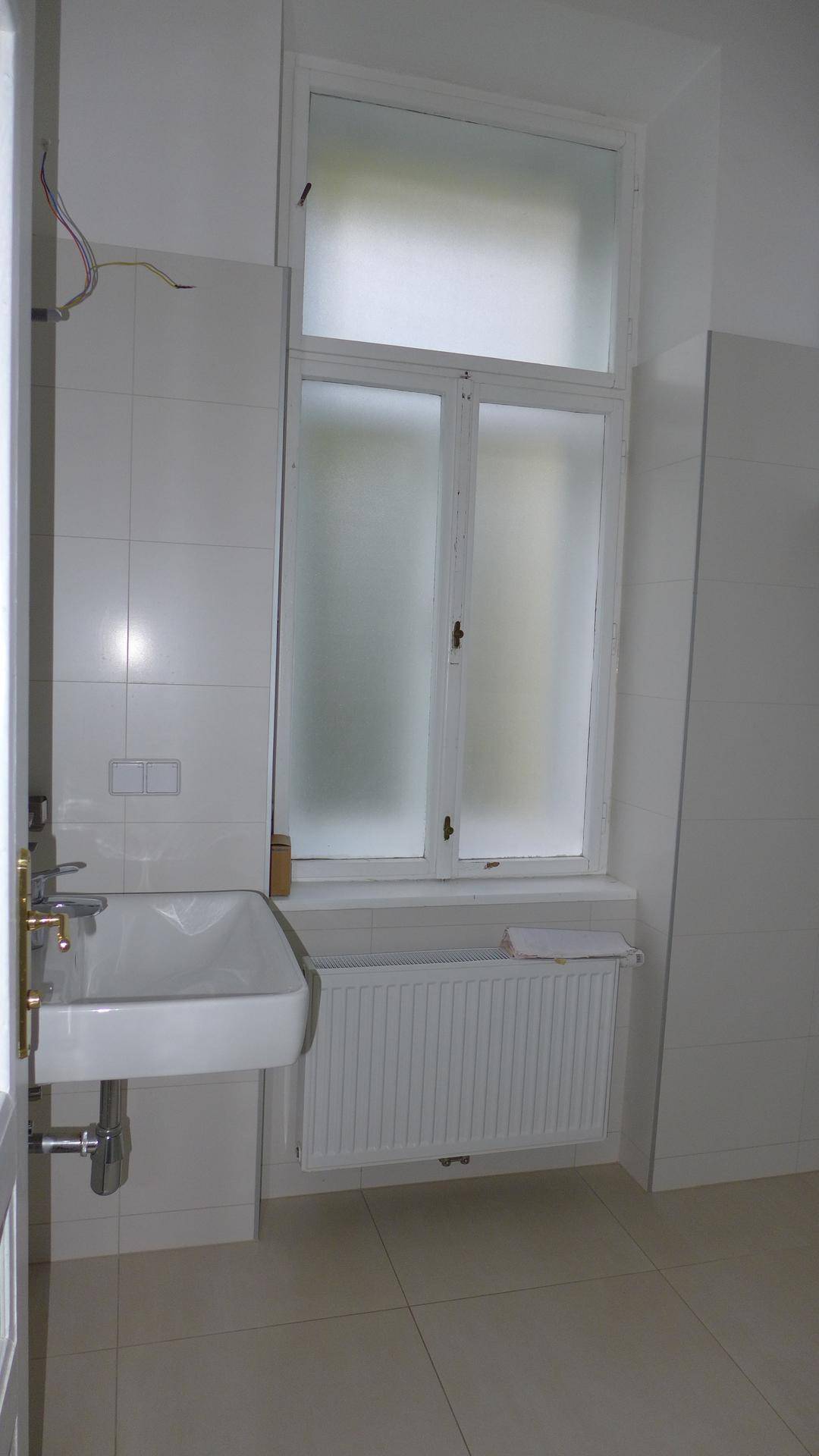 Badezimmer mit weiß gefliesten Wänden, Waschbecken und einem Fenster mit Milchglas.