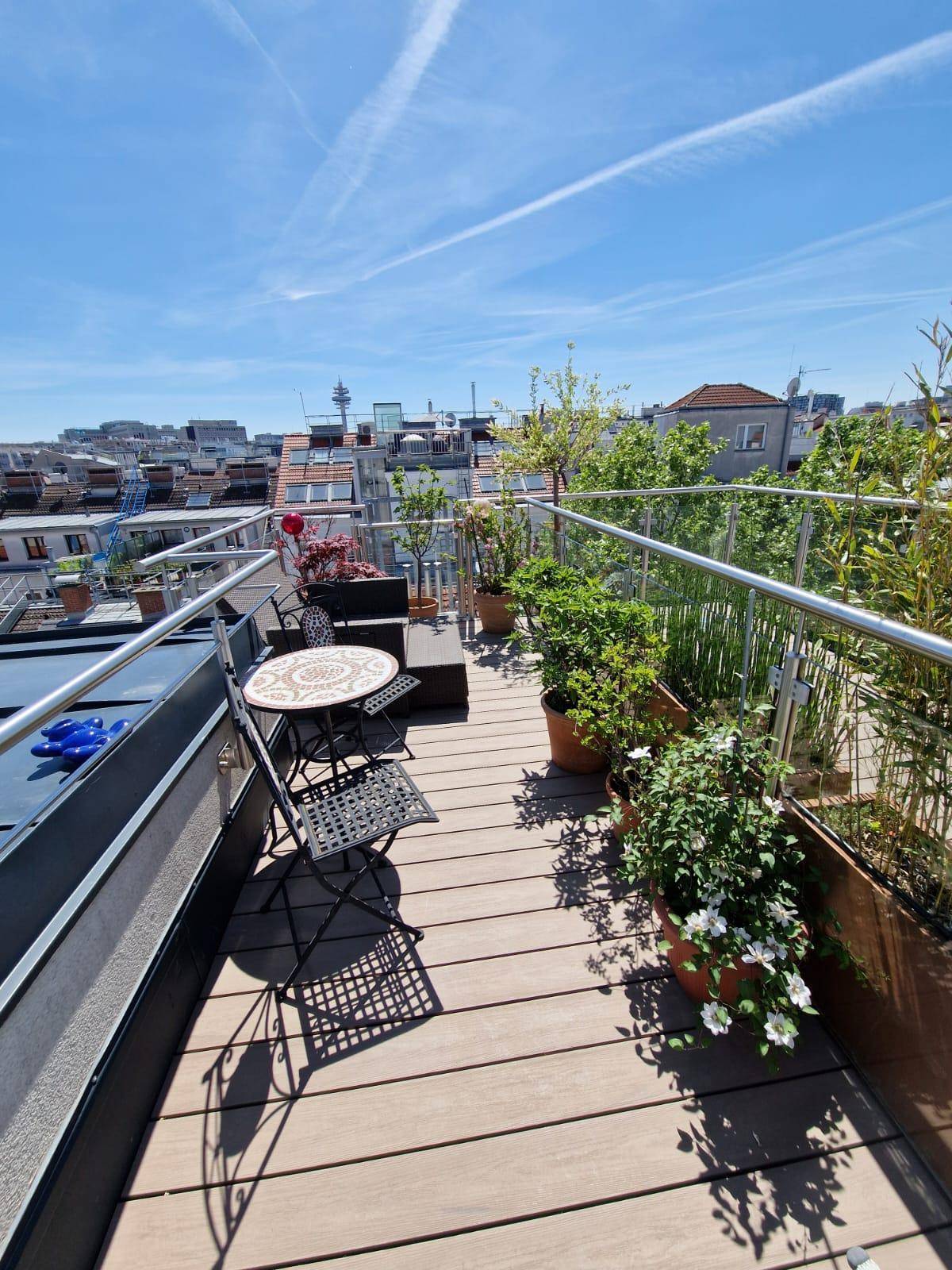 Weitläufige Dachterrasse mit Holzboden, vielen Pflanzen und einem weiten Blick über die Stadt.