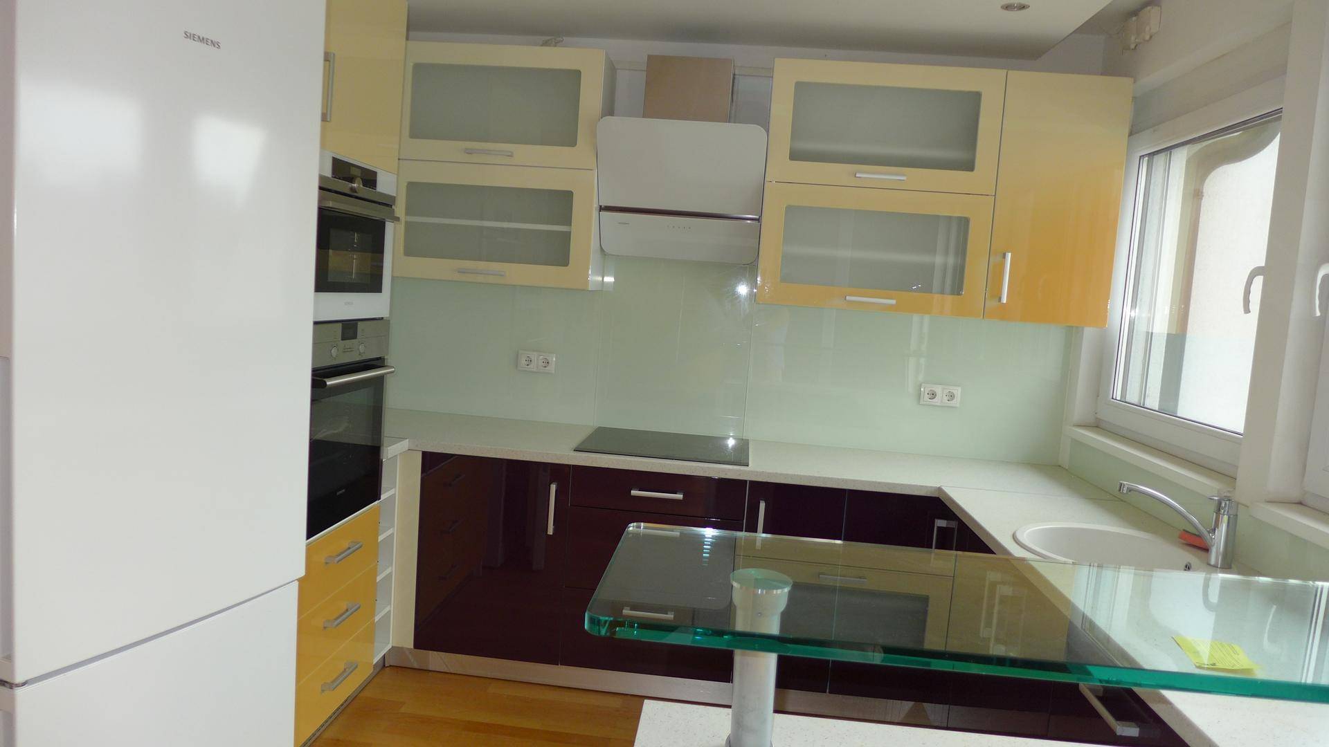 Moderne Einbauküche mit hellen und dunklen Schränken, integrierten Geräten und einer Glas-Frühstücksbar.