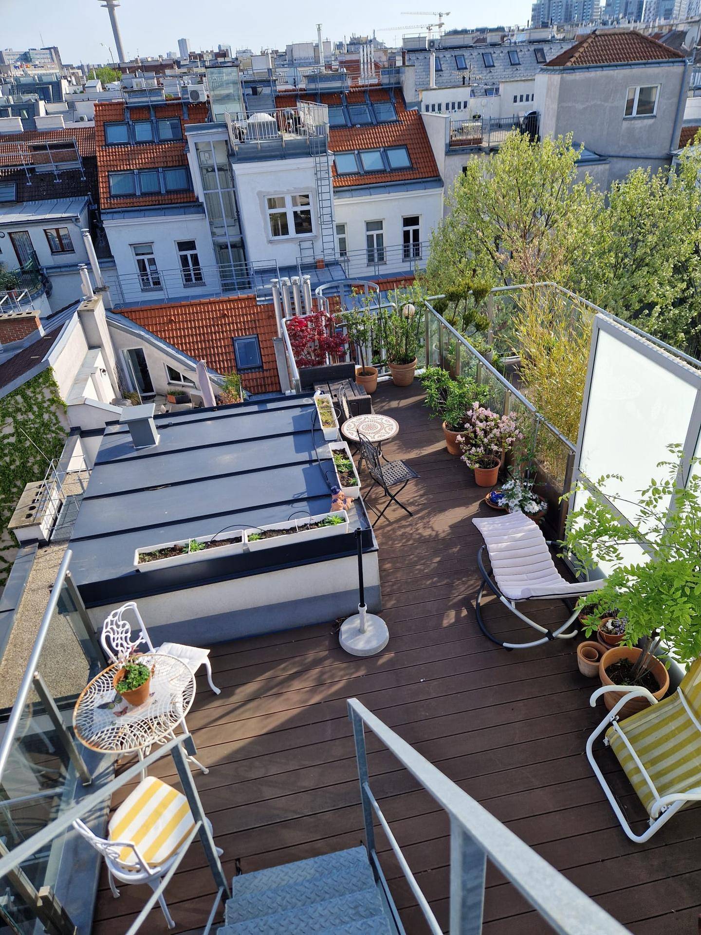 Große Dachterrasse mit verschiedenen Sitzbereichen, Holzboden und Panoramablick über die Stadt.