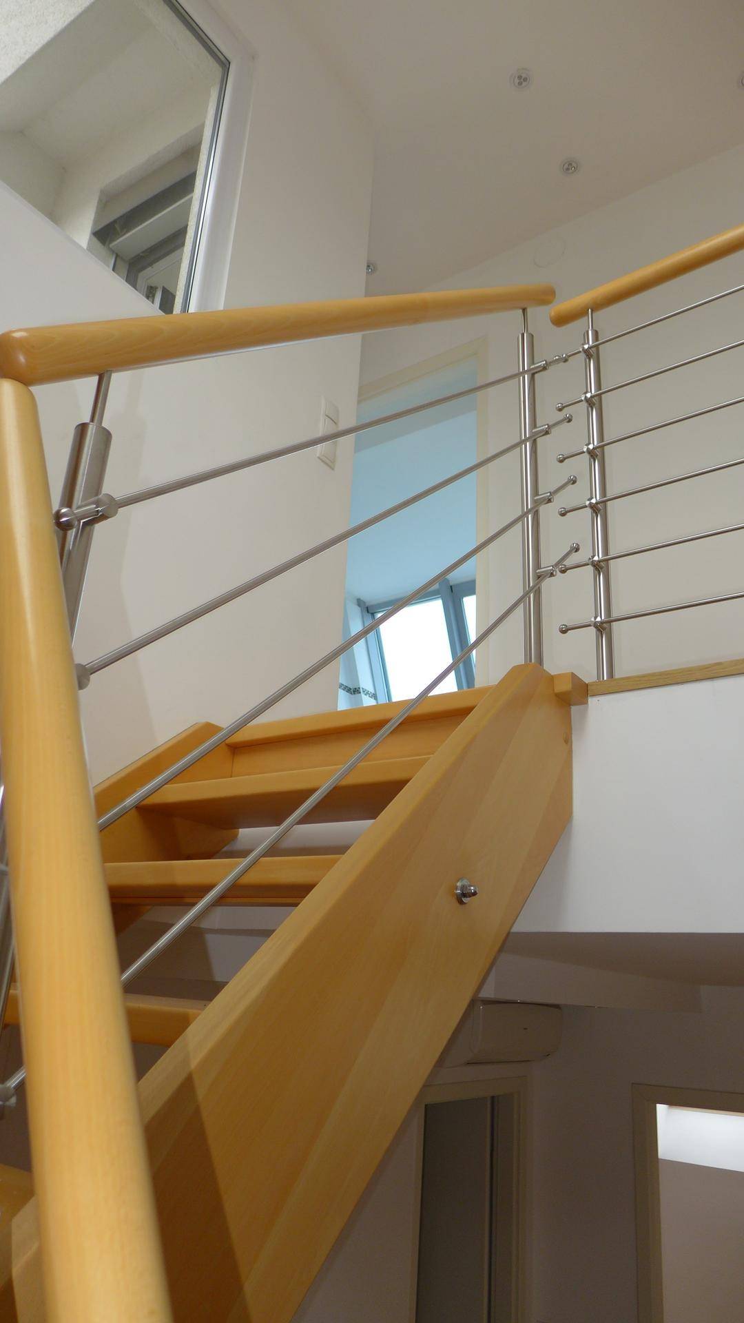 Detailansicht einer modernen Holztreppe mit schlanken Metallgeländern und heller Umgebung.