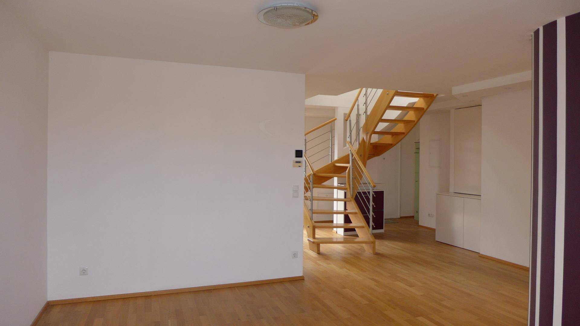 Heller Wohnbereich mit elegantem Holzparkett und einer modernen Wendeltreppe mit Metallgeländer.