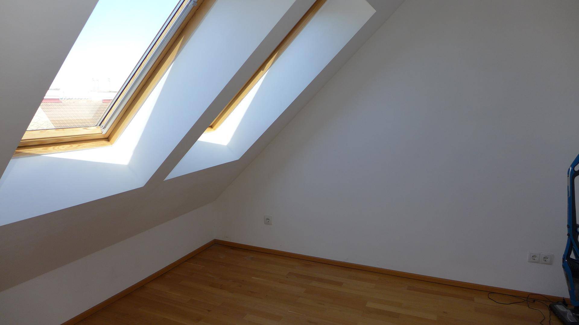 Lichtdurchfluteter Raum im Dachgeschoss mit zwei großen Dachfenstern und hellem Holzparkett.