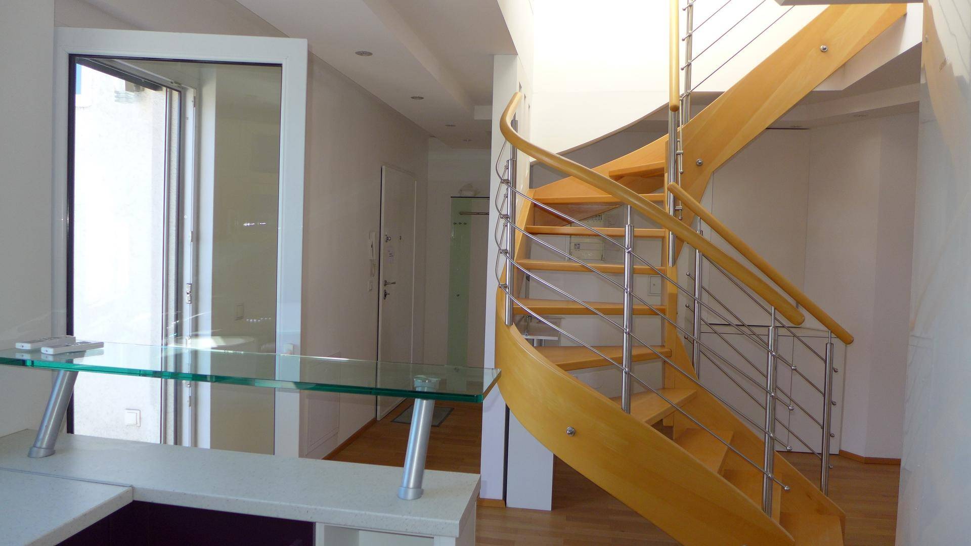 Heller Eingangsbereich mit einer eleganten Holzwendeltreppe und einer modernen Glasablage.